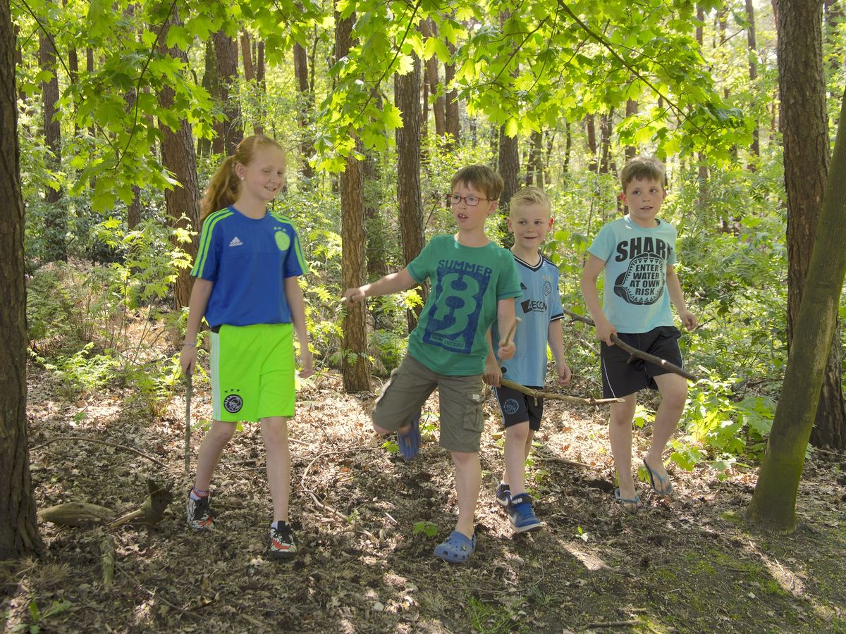 Vier kinderen lopen met een stok door het bos bij de hutten