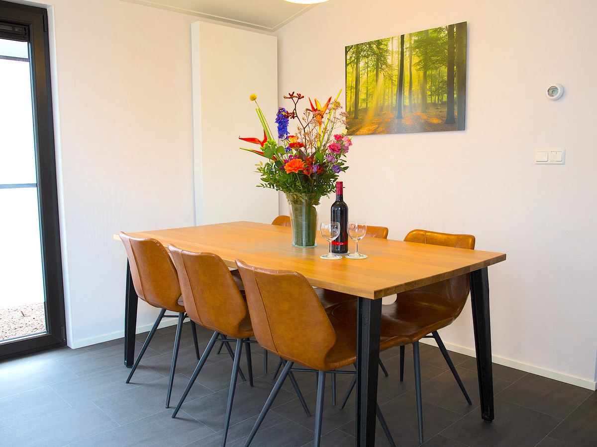 De eettafel in de boslodge met zes stoelen en een schilderij van het bos
