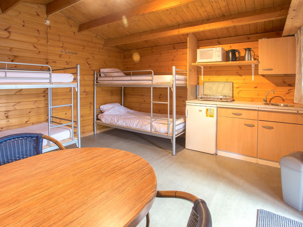 Binnen in de blokhut: een stapelbed, het keukenblok met koelkast en een ovale tafel