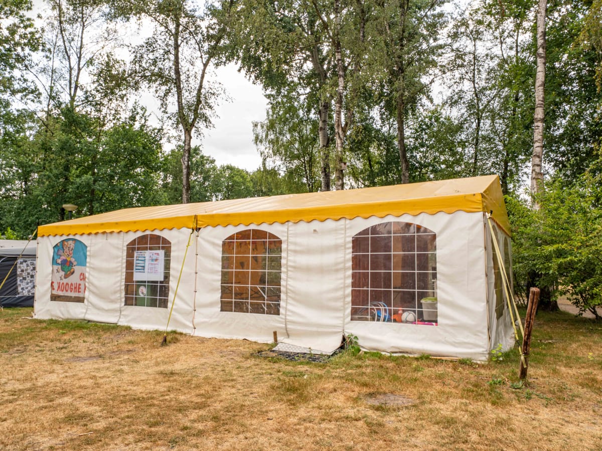 De geel met witte animatietent tussen de bomen aan de rand van het veld