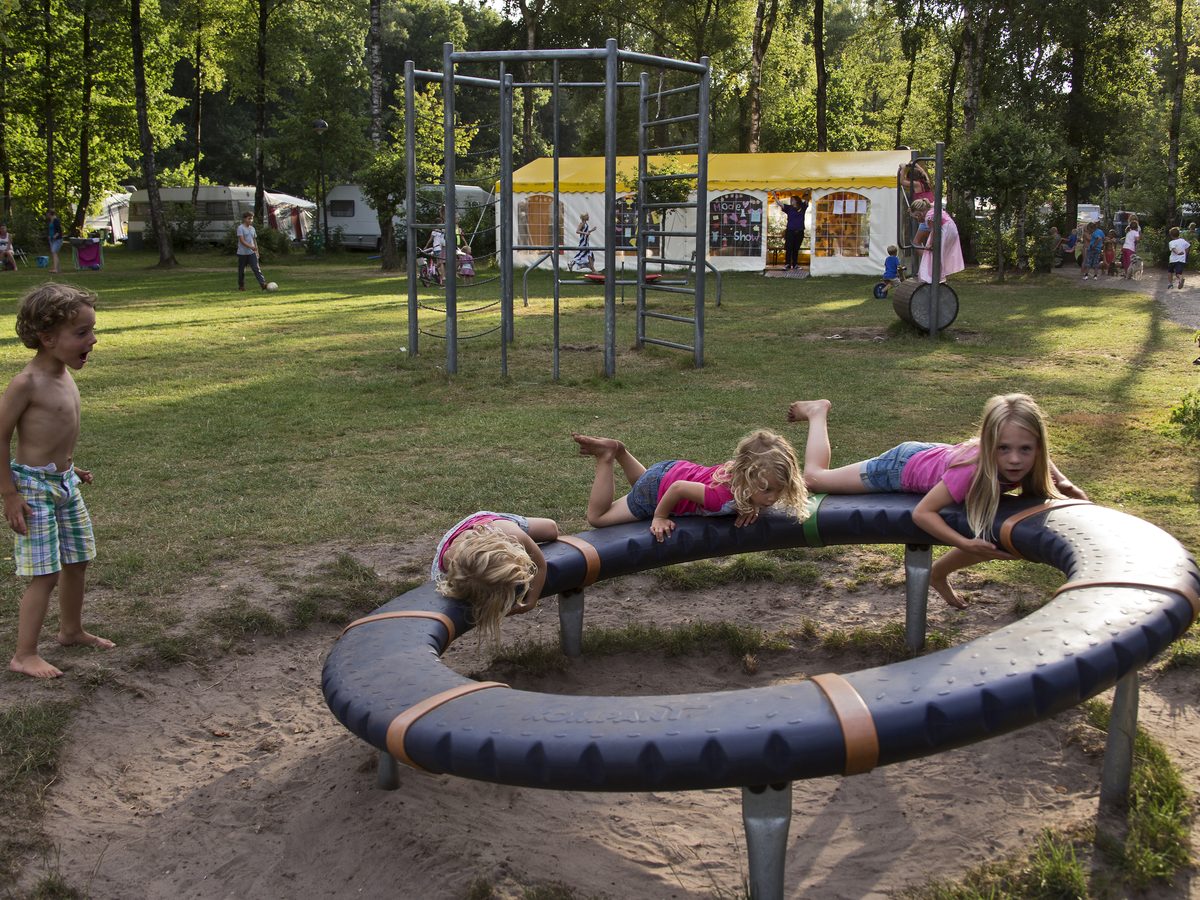 Kinderen hangen over de rand van het draaitoestel in het zand