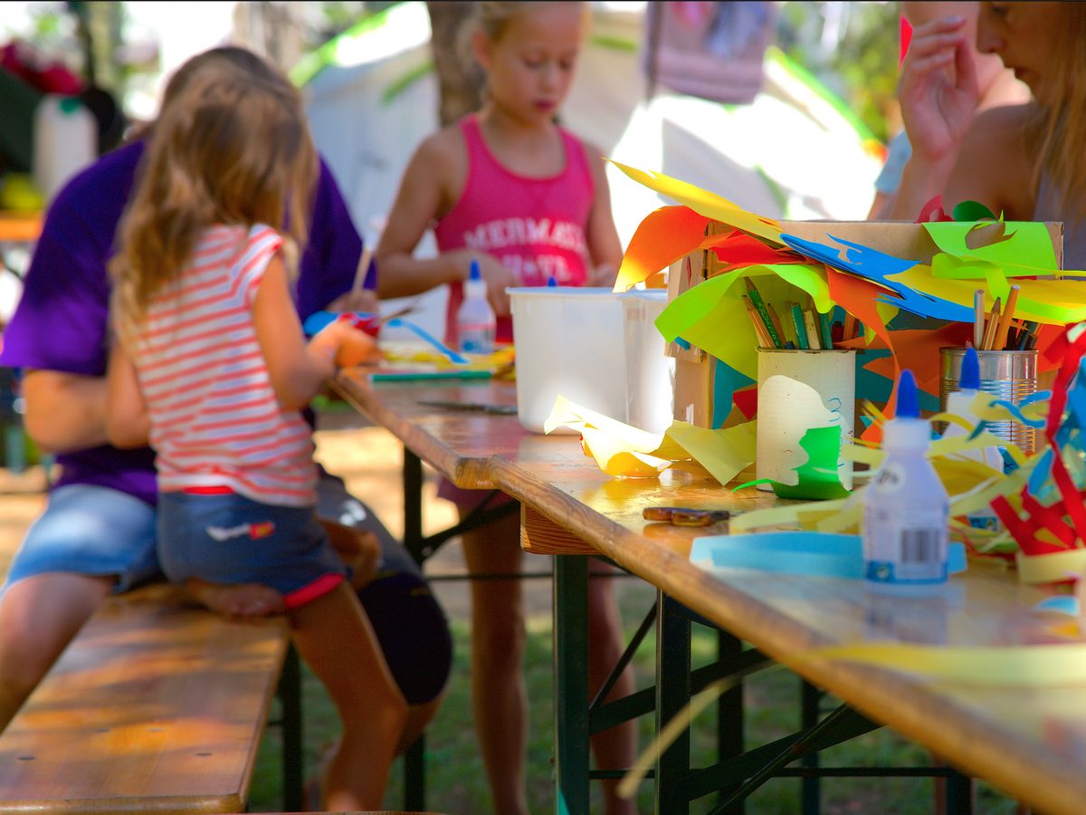 Kinderen knutselen aan een lange tafel met gekleurd papier en lijm