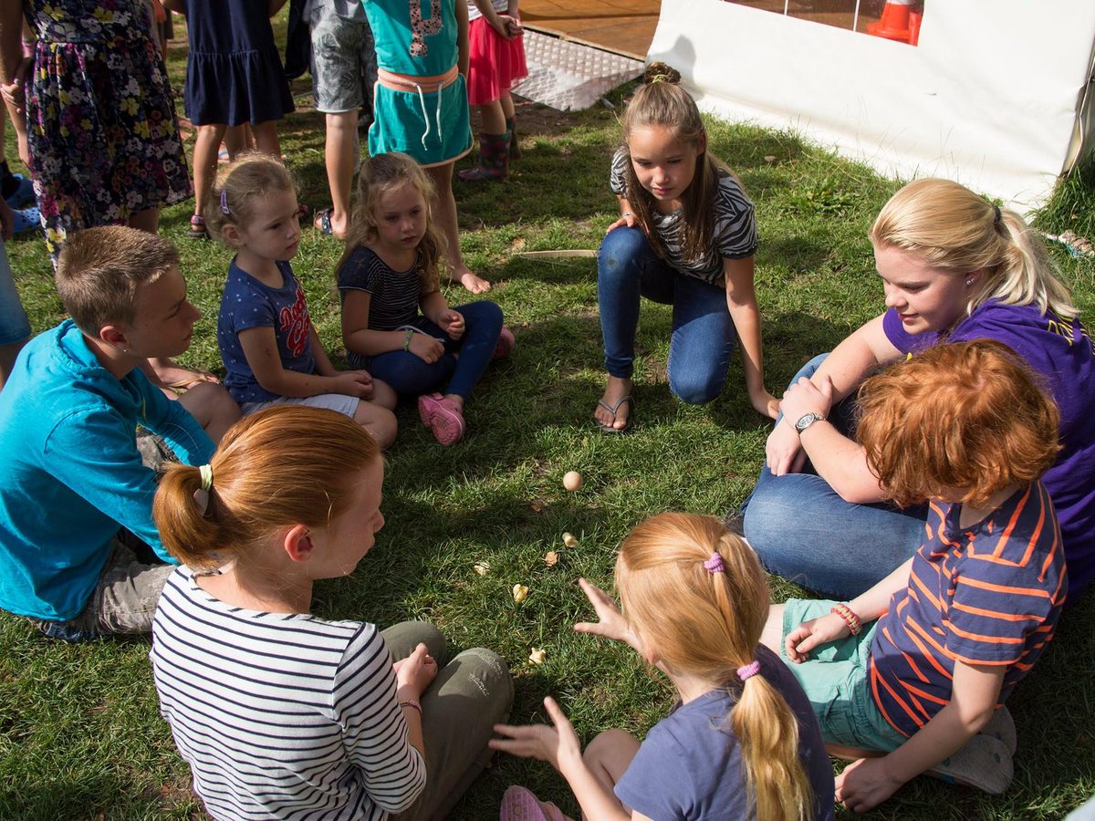 Kinderen zitten in een kring in het gras met iemand van het animatieteam