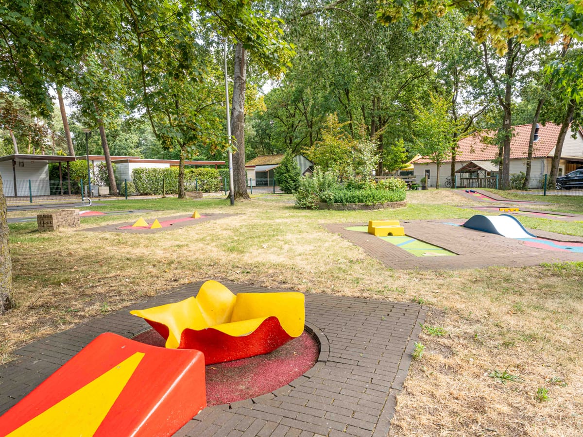 De midgetgolfbaan met kleurrijke hindernissen tussen het gras onder de bomen