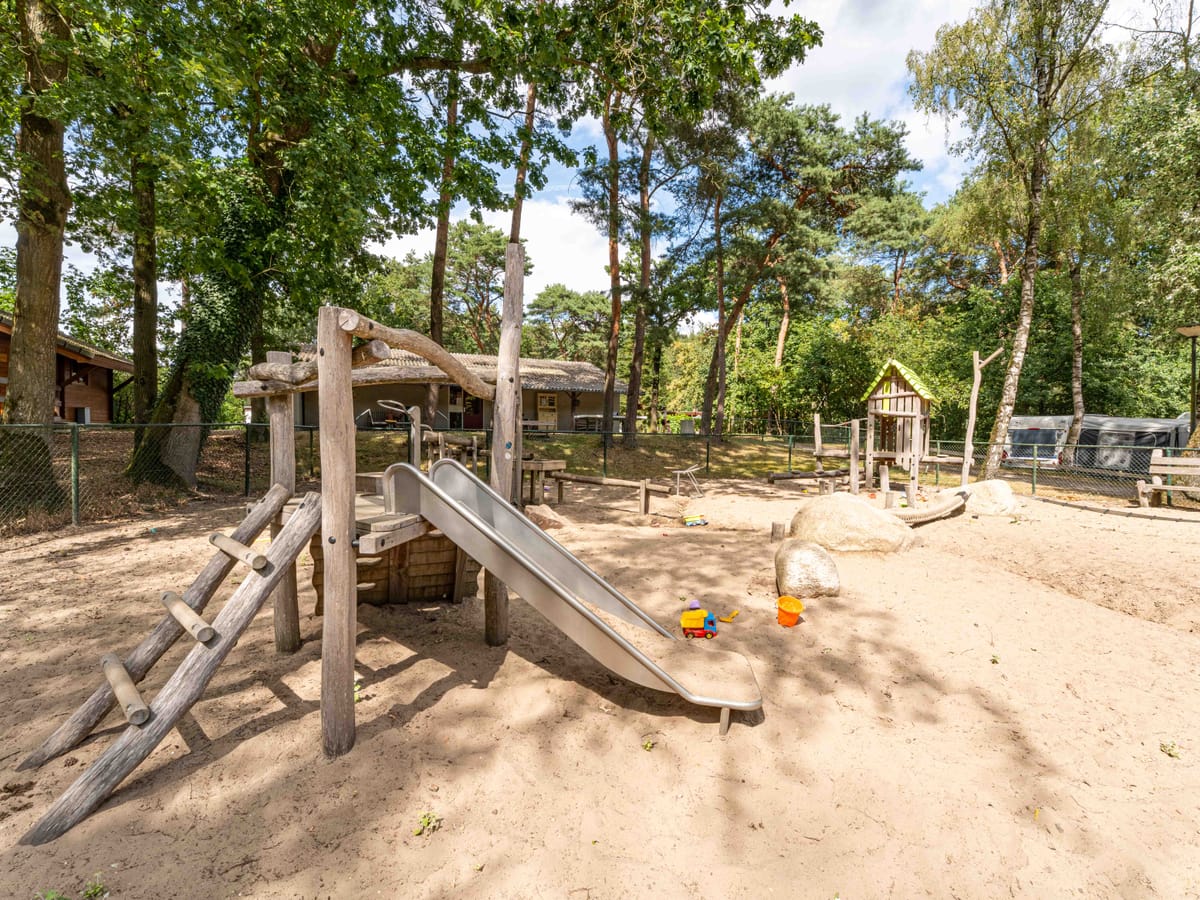 De natuurspeeltuin met een houten klimtoestel en een glijbaan in het zand