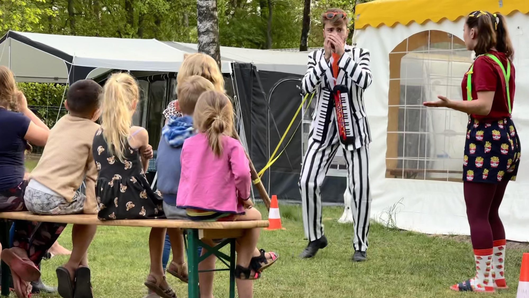 Kinderen kijken op de banken naar twee verklede spelers voor de animatietent