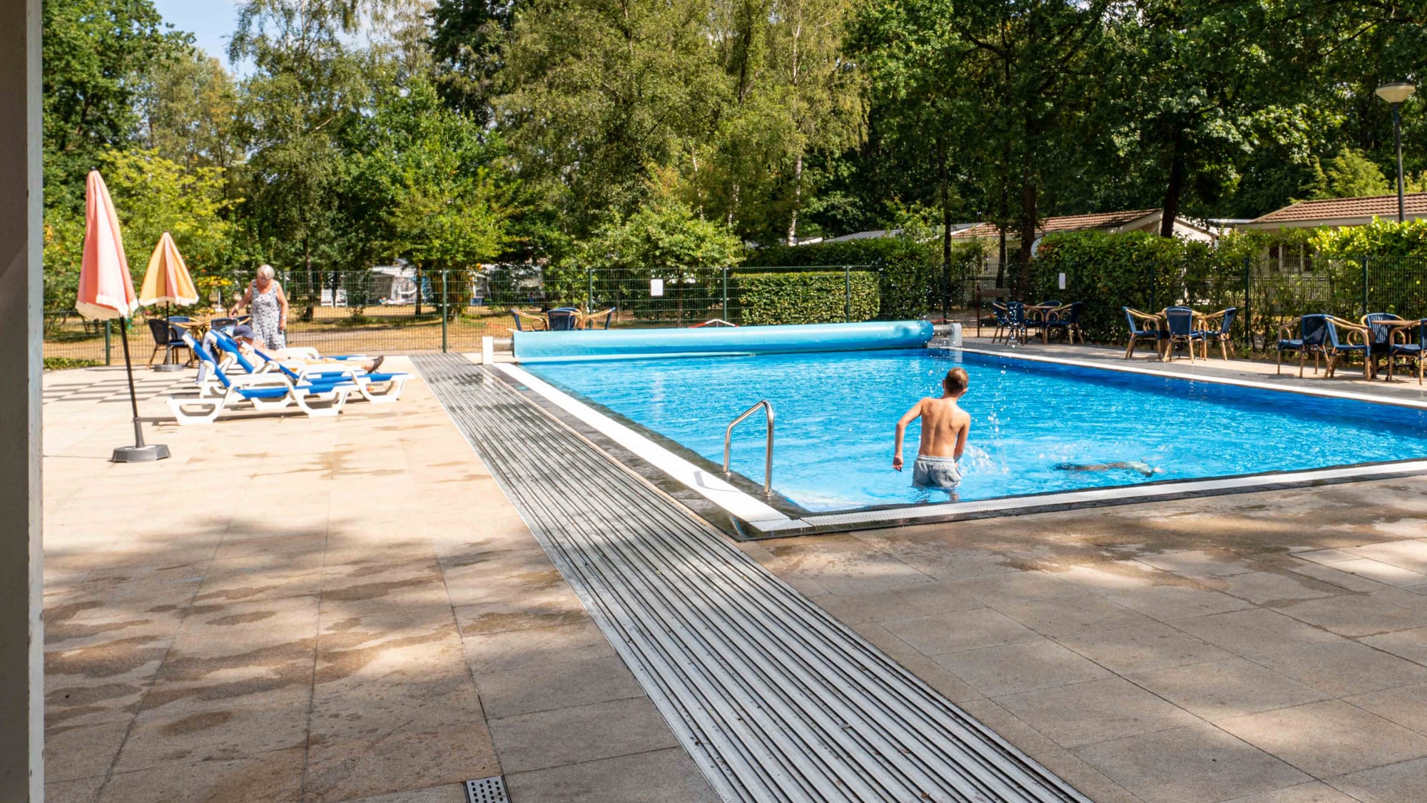 Een jongen speelt in het water van het buitenzwembad, met ligbedden op het terras