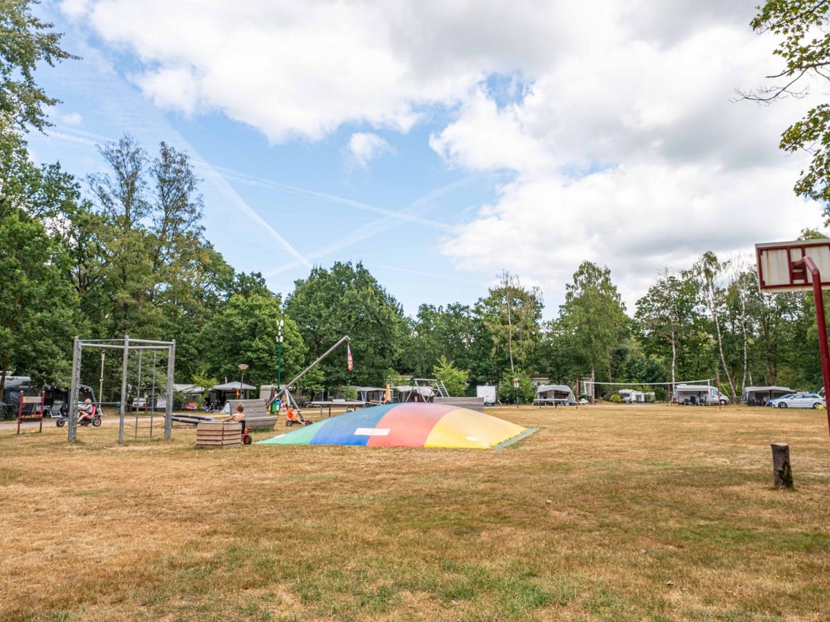 Het open speelveld met het springkussen en caravans langs de bosrand