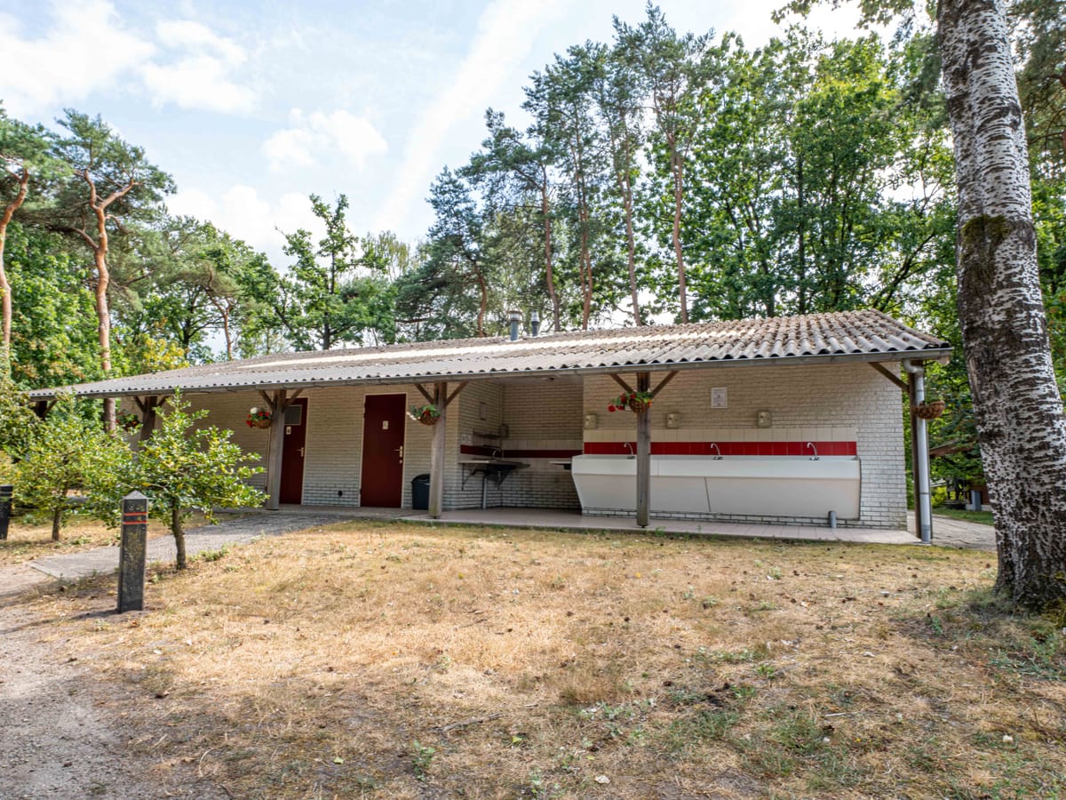 Het sanitairgebouw met een overdekte gang langs de voorkant en bomen erachter
