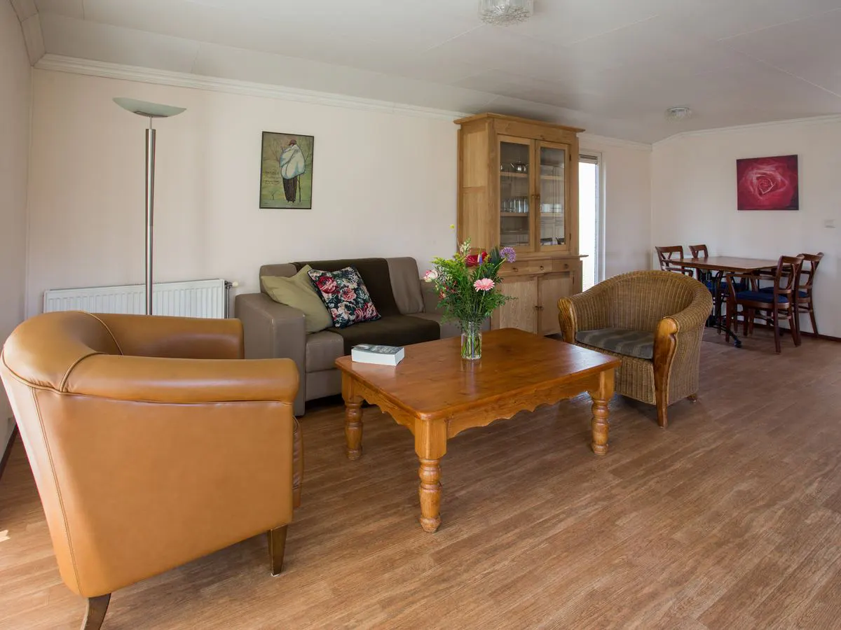 De woonkamer van het chalet met een bank, twee fauteuils en een eettafel achterin