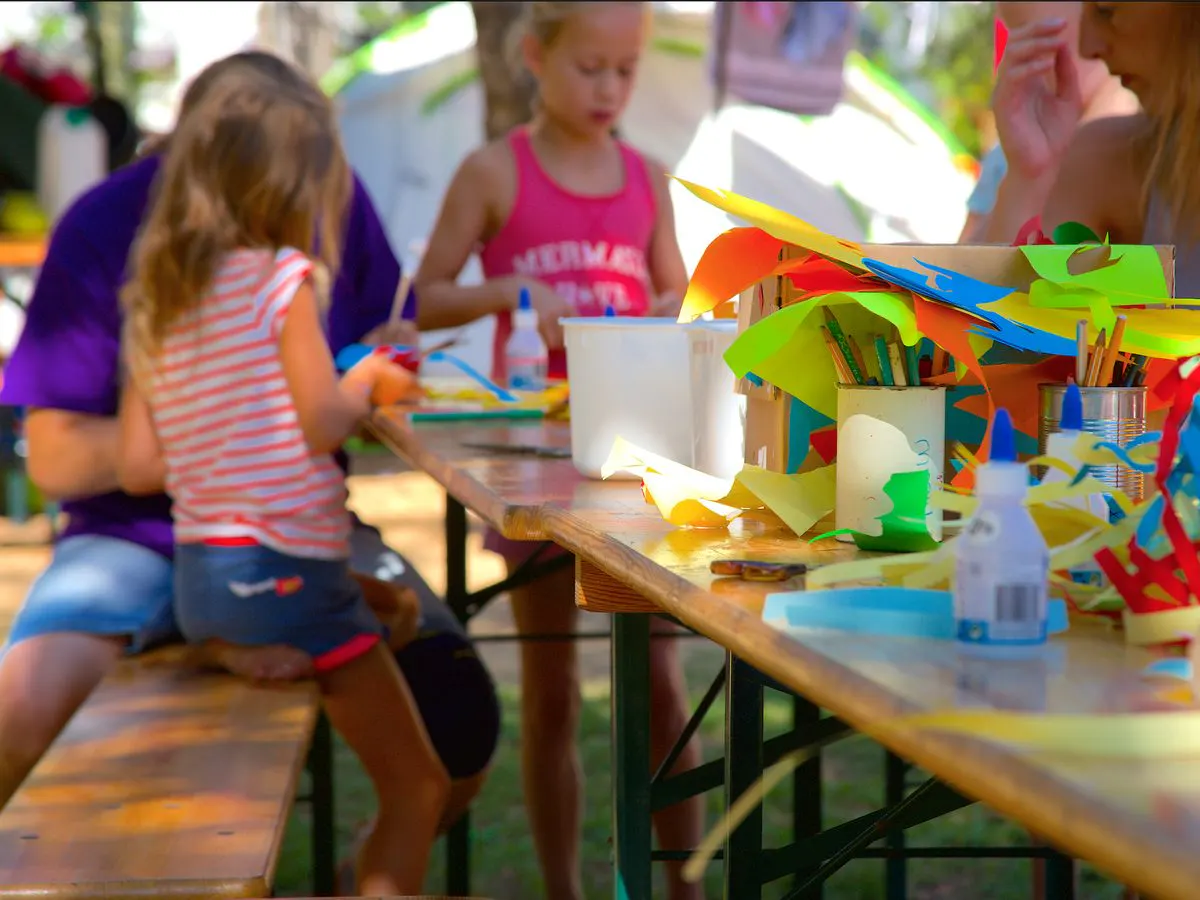 Kinderen knutselen aan een lange tafel met gekleurd papier en lijm