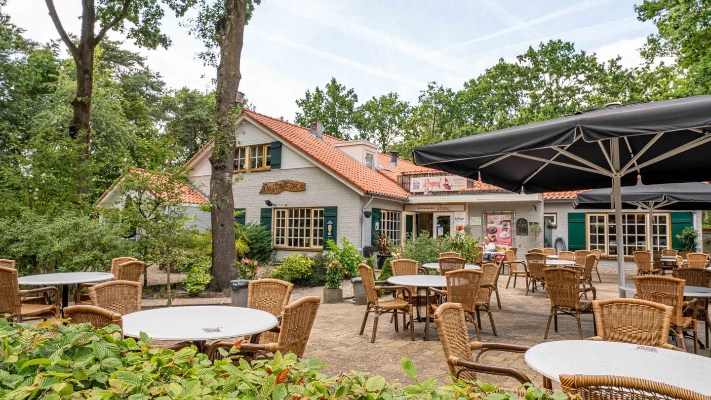 Het terras van het pannenkoekenhuis met rieten stoelen, grote parasols en gasten aan de tafels
